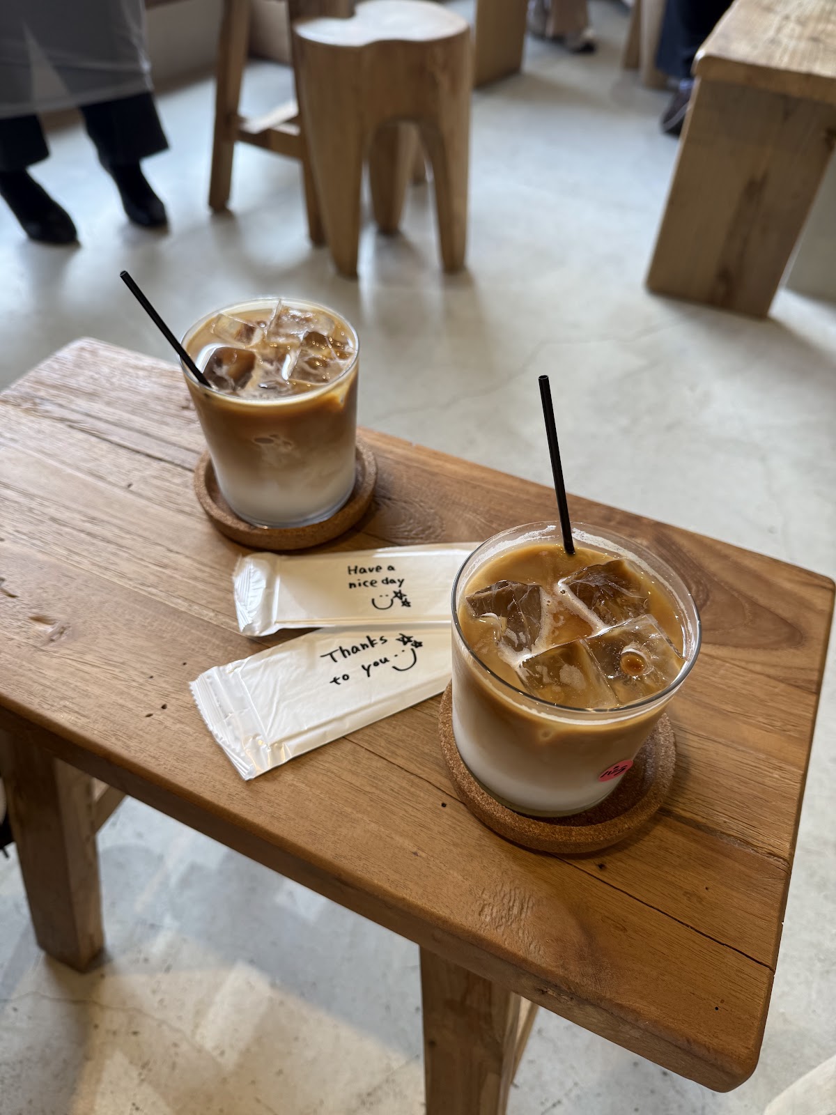 木製テーブルの上に置かれた2杯のアイスラテと、手書きで「Have a nice day」「Thanks to you」と書かれたストロー袋